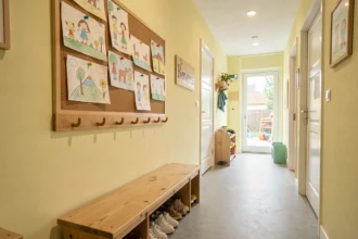 Couloir d'entrée d'une crèche en Finistère avec dessins d'enfants, petits crochets en bois et chaussures alignées sous un banc