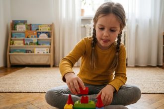 Jeune fille concentrée construisant un château avec des briques en plastique colorées sur le parquet d'un salon