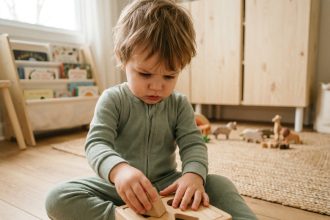 Enfant en bas âge concentré sur un jouet de tri de formes en bois dans une salle de jeux scandinave
